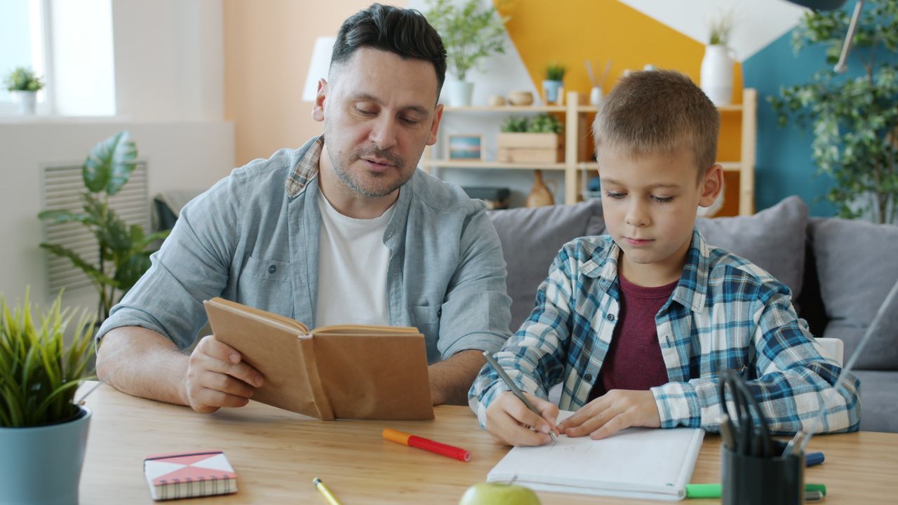 Father helping son with homework in a cozy living room setting, promoting education and bonding.