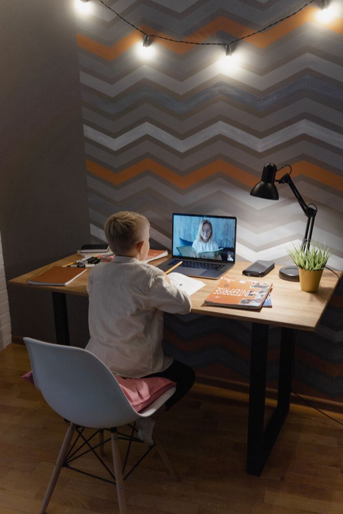 A young boy engaged in a virtual class at a modern desk setting with warm ambient lights.